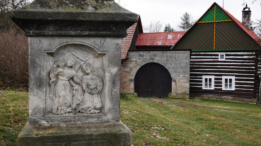 Podstavec pod sochou je novější. Pochází z roku 1884, kdy ho na přání manželů Františka a Petronily Jirošových zhotovil a čtyřmi reliéfy opatřil Josef Zeman z Tatobit.