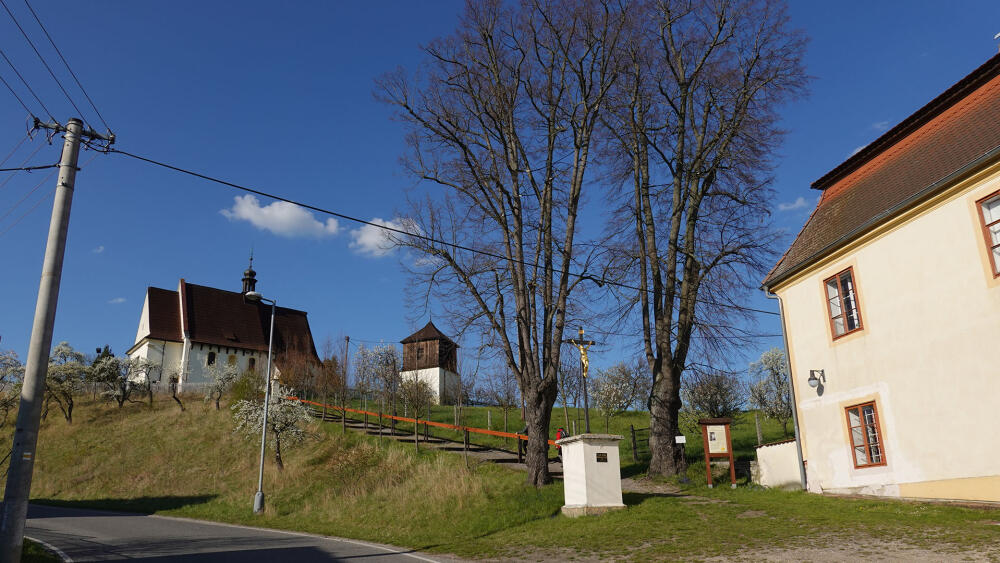 Kostel, zvonice a zlatý kříž z roku 1868 vedle rohu barokní fary.
