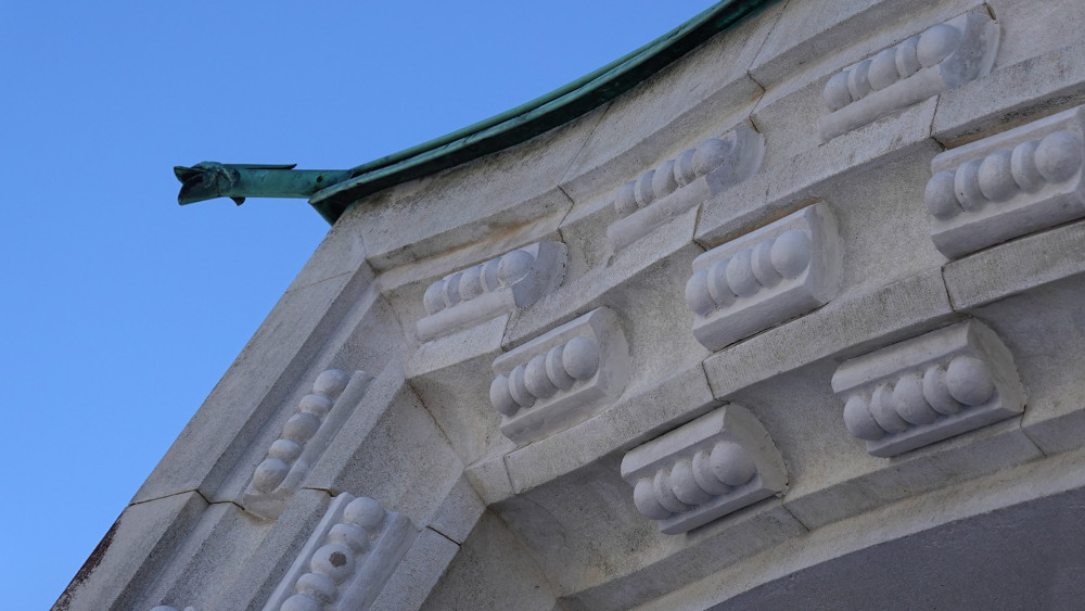 Korunní římsu v šířce reliéfu dekoruje zubořez.  