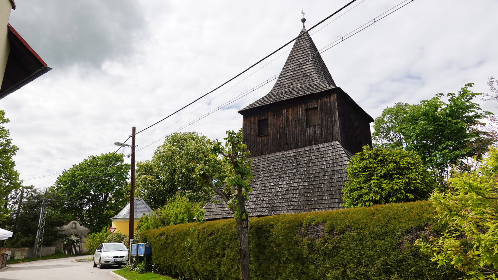 Na rozdíl od kostela je zvonice opravdovou dominantou Vlastibořic. V pozadí je vidět brána do Melicharova statku. Na jeho pozemku stávala tvrz ze 14. století.