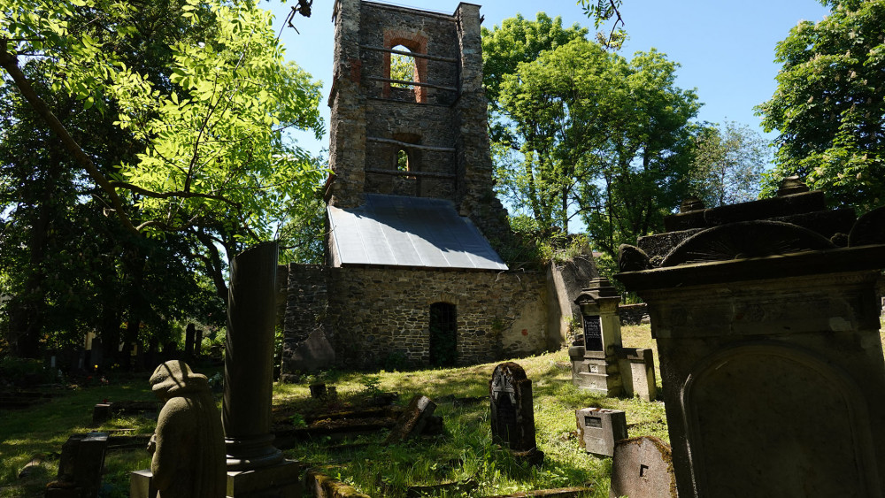 Zvonice stojí uprostřed ostudně zanedbaného a vandaly poničeného hřbitova.