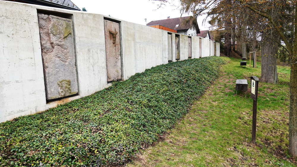 Náhrobky zasazené do betonové zdi, připomínka starého hřbitova.