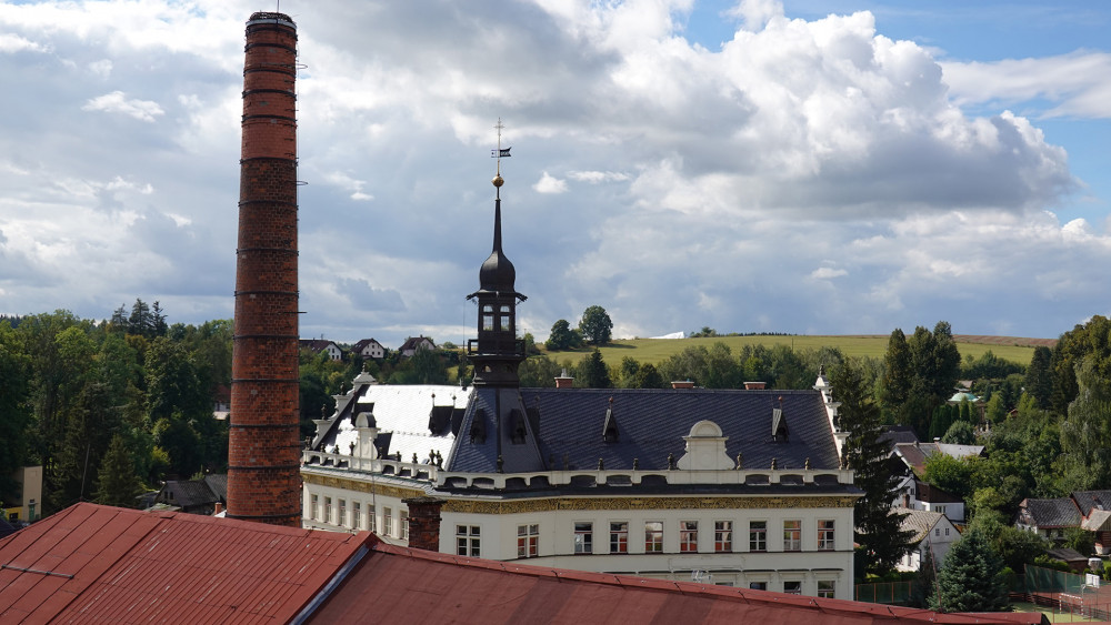 Pohled na věž a břidlicovou střechu školy z hvozdu bývalého pivovaru. 